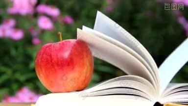 一个苹果放在花园里的一本书上，风吹着，书的书页翻了起来